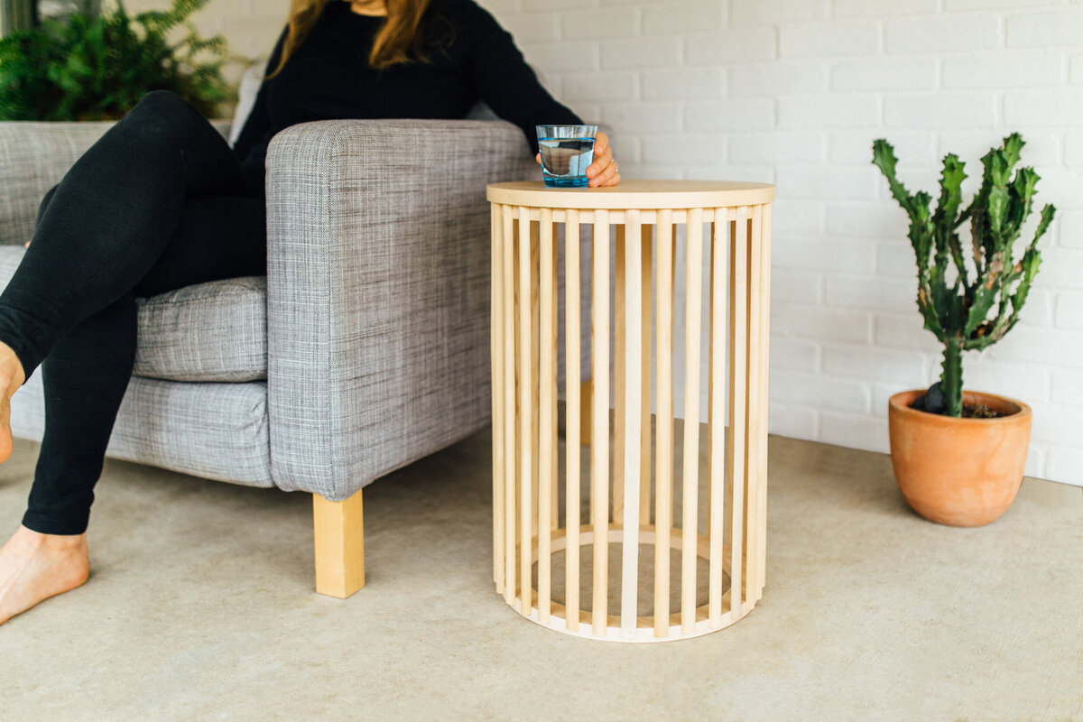 A woman sets her water glass on a side table supported by vertical wooden dowels