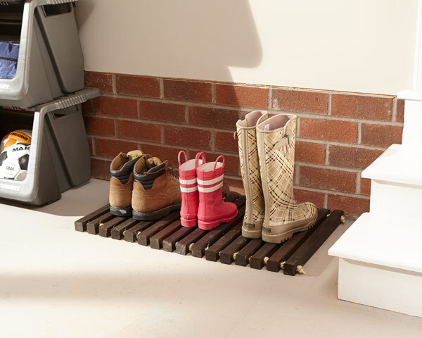 Rain boots lined up on a doormat made of square wooden dowels tied together with rope