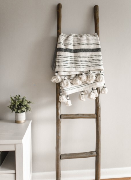 a throw blanket hangs on a decorative ladder made up of wooden dowels