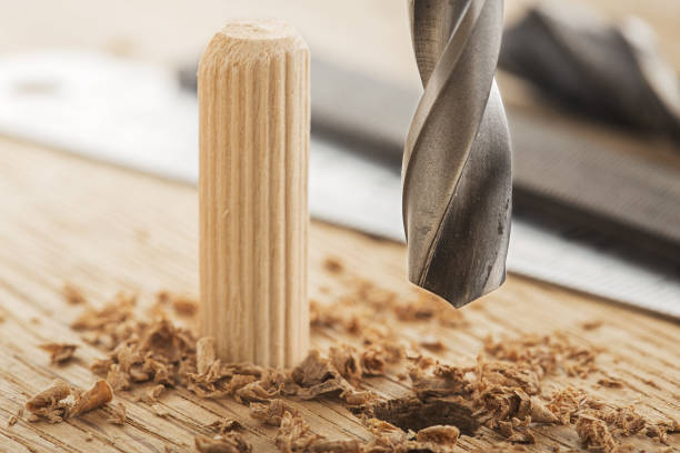 A drill bit being drilled into a piece of wood with a dowel peg in a nearby hole