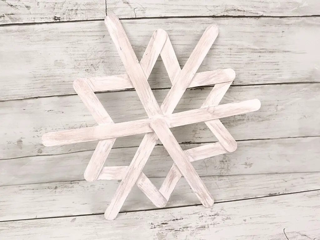 A white snowflake made of popsicle sticks on a wood surface